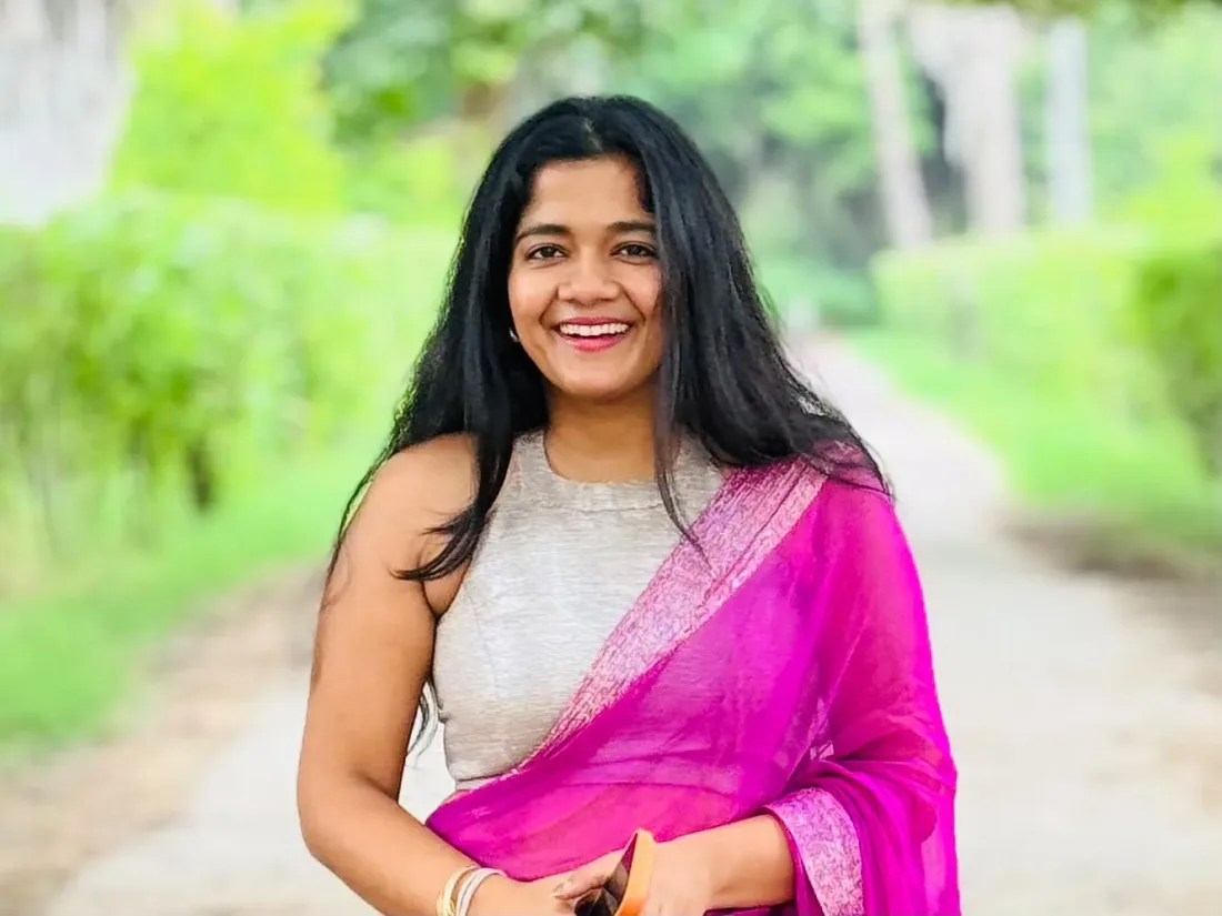 Cheshta Agarwal, founder and host of The Trip Keeper, smiling on a green country road